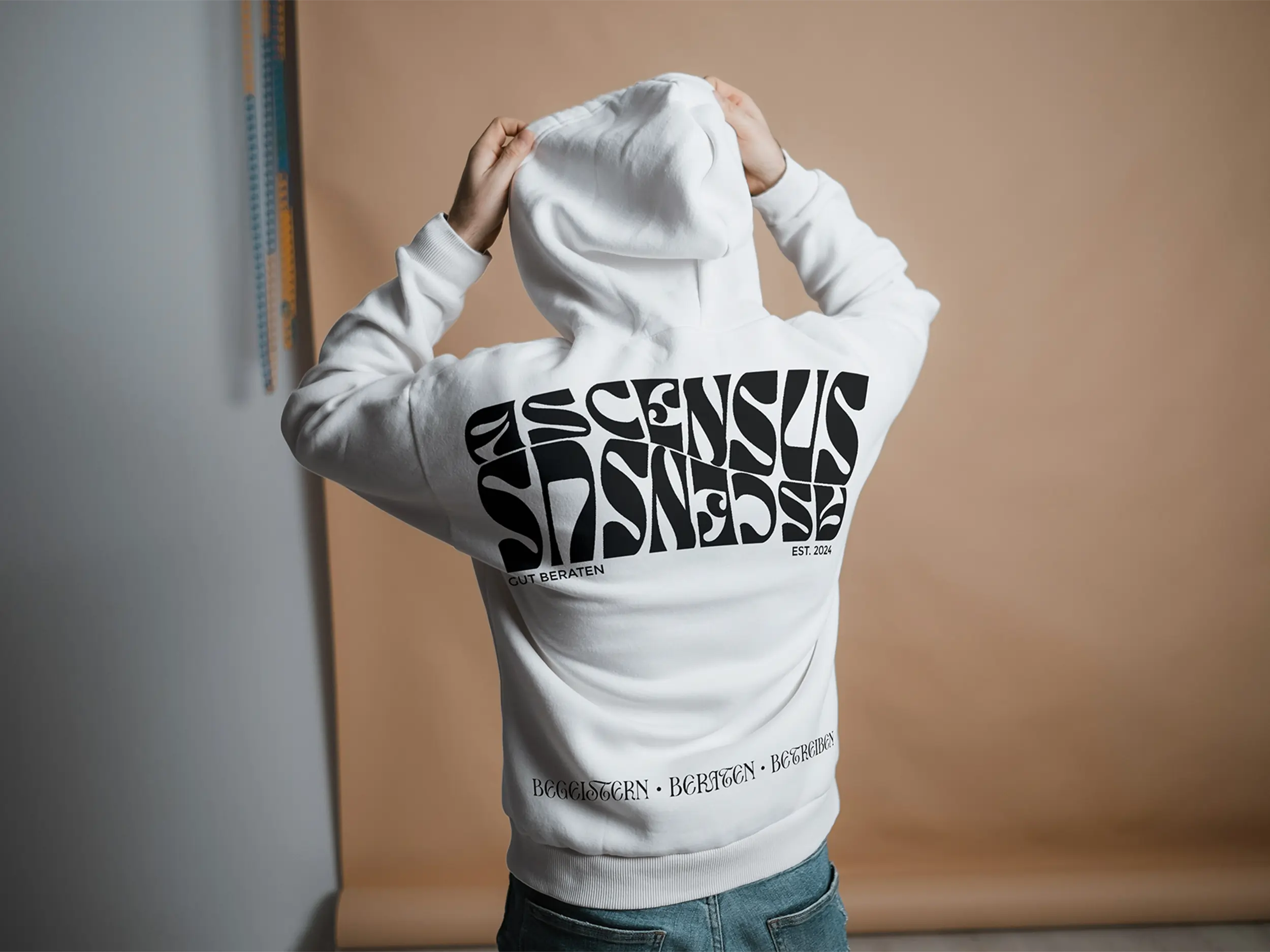 Eine Person mit einem weißen Ascensus Hoodie dreht der Kamera den Rücken zu.